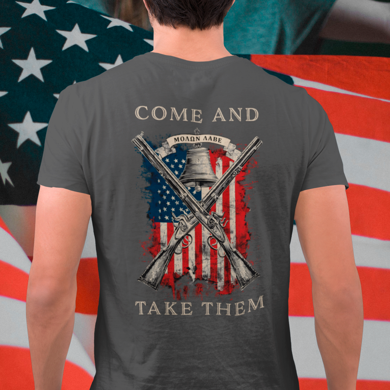 rear view of a mean standing in front of a USA flag wearing a patriotic shirt white color fabric tee with logo on front and american flag with liberty  bell and crossed rifles on back, motto that states Come and Take Them  and molon labe on scroll