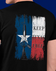 rear view of a man wearing a black colored fabric shirt standing in front of an american flag with americantees.us logo on front and Texas flag with rifle and Keep Texas Free writing on back