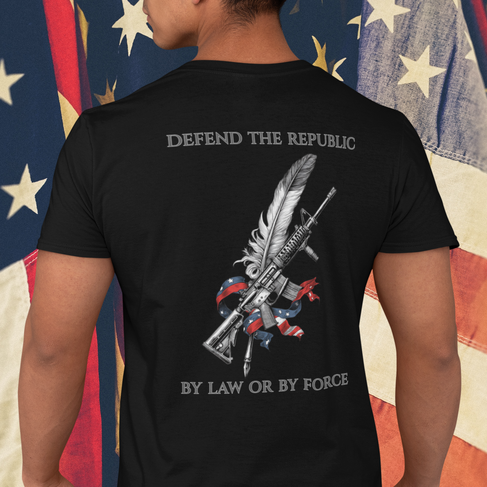 Patriotic Person wearing a black t-shirt with a graphic design of a rifle  crossed with a quill fountain pen and an American flag ribbon, with the quote Defend the Republic by law or by force.