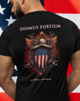 man standing in front of a flag wearing a patriotic shirt front view black color fabric tee logo with eagle on front, american flag on shield with scrollwork, Domus Fortium, home of the brave motto