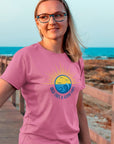 high-tides-and-good-vibes-charity-pink-t-shirt-beach-sunset-unisex-mockup-of-a-woman-with-glasses-standing-on-a-bridge-by-the-beach