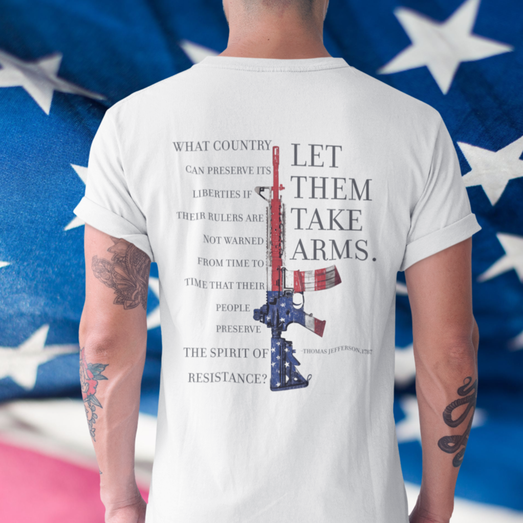 rear view of a man standing in front of an American flag wearing a white color fabric patriotic shirt with americantees.us logo on front and Thomas Jefferson quote on back.