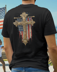 Person wearing a black t-shirt with a cross and American flag design, standing on a beach.