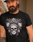 warlord-design-skull-with-feathered-headress-black-t-shirt-mockup-featuring-a-bearded-man-leaning-against-a-rusty-wall