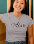 alive-out-of-spite-athletic-heather-grey-t-shirt-funny-mockup-of-a-woman-with-a-heather-tee-sitting-against-a-wooden-background