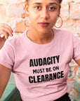 audacity-must-be-on-clearance-pink-t-shirt-unisex-funny-mockup-of-a-beautiful-girl-sitting-on-a-rustic-wooden-chair