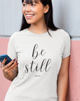 be-still-psalm-46-10-white-t-shirt-womens-christian-inspiring-tee-mockup-featuring-a-woman-leaning-against-a-pink-and-white-wall
