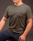 dignified-until-the-green-flag-drops-army-green-mens-t-shirt-crew-neck-tee-mockup-of-a-guy-in-blue-trousers-sitting-on-a-stool-against-a-dark-gray-wall