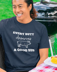 every-butt-deserves-a-good-rub-navy-blue-t-shirt-with-pig-graphic-barbeque-cooking-unisex-crewneck-tee-mockup-featuring-a-smiling-man-by-a-grill-at-a-bbq-party