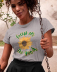 focus-on-the-good-sunflower-athletic-heather-grey-t-shirt-womens-mockup-of-a-heathered-tee-of-a-woman-on-a-swing