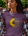 in-a-world-full-of-roses-be-a-sunflower-team-purple-t-shirt-womens-mockup-of-a-young-woman-standing-in-front-of-a-green-wall