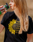 take-every-chance-drop-every-fear-black-t-shirt-sunflower-mockup-of-a-woman-wearing-a-tee-while-drinking-water-at-a-park