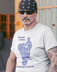 the-brave-dont-live-forever-white-t-shirt-mockup-featuring-a-tattooed-middle-aged-biker-leaning-on-a-motorcycle-outside-a-bar