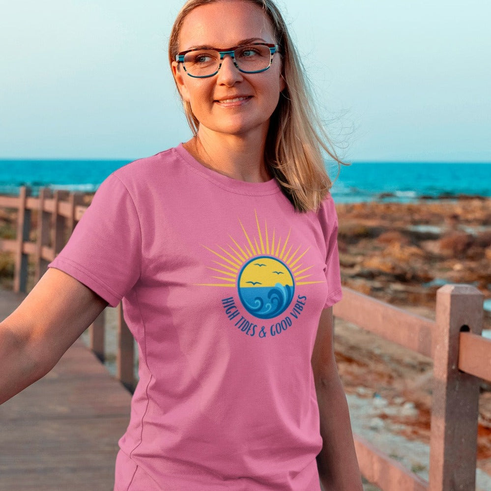 high-tides-and-good-vibes-charity-pink-t-shirt-beach-sunset-unisex-mockup-of-a-woman-with-glasses-standing-on-a-bridge-by-the-beach