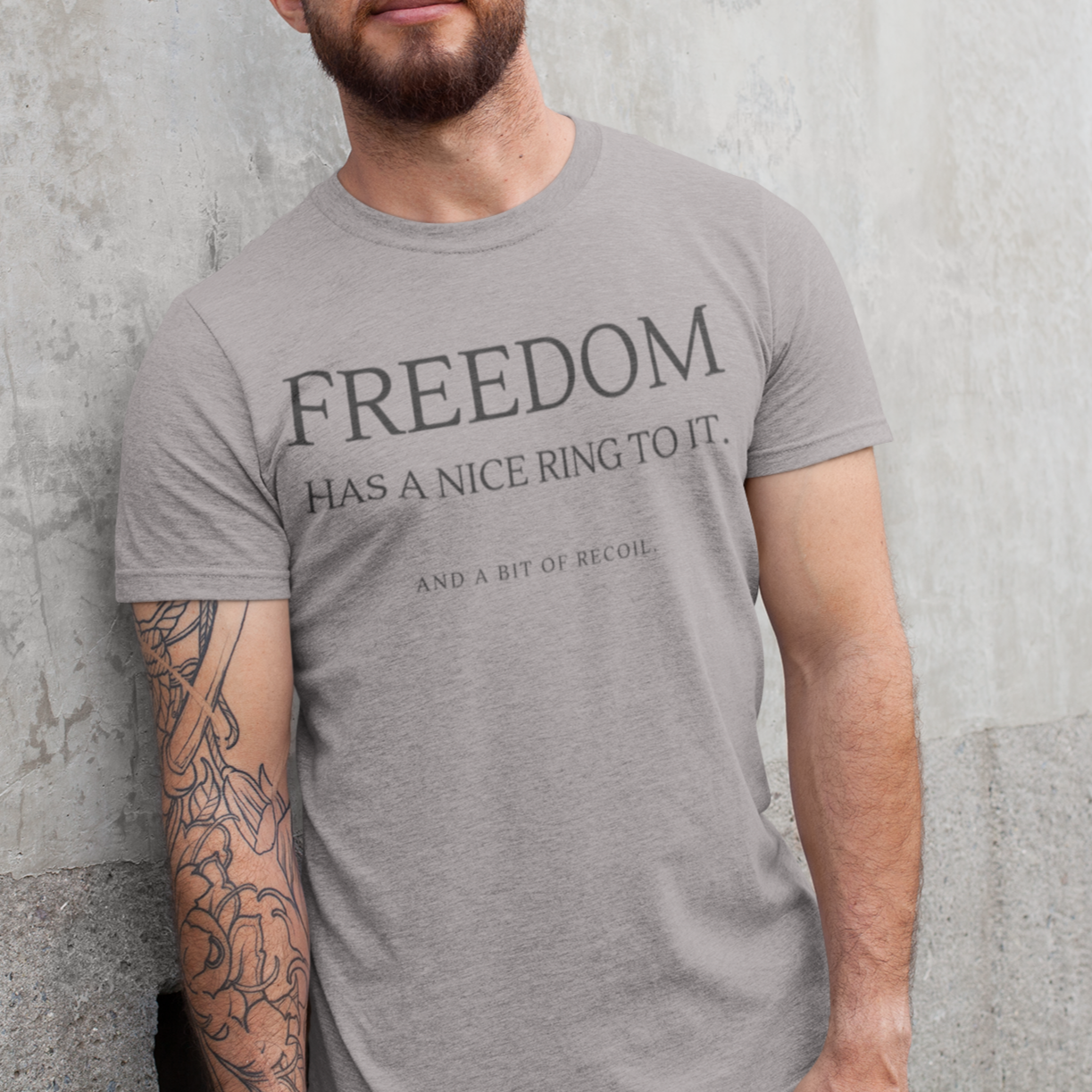 freedom-has-a-nice-ring-to-it-and-a-bit-of-recoil-athletic-heather-grey-t-shirt-2a-heathered-tee-mockup-of-a-man-leaning-against-a-concrete-wall