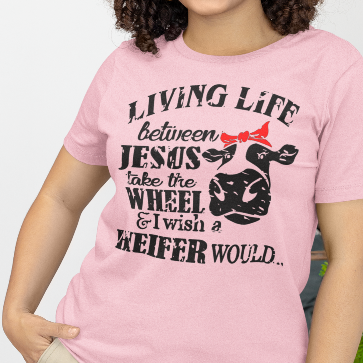 living-life-between-jesus-take-the-wheel-and-i-wish-a-heifer-would-pink-t-shirt-bella-canvas-tee-mockup-featuring-a-smiling-woman-with-curly-hair