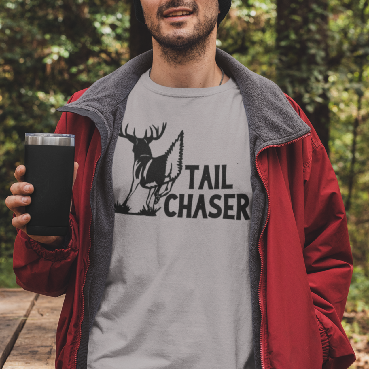 tail-chaser-athletic-heather-grey-t-shirt-mockup-featuring-a-man-holding-a-20-oz-travel-mug-in-the-woods