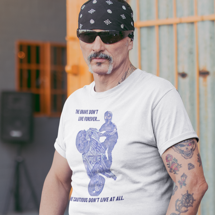 the-brave-dont-live-forever-white-t-shirt-mockup-featuring-a-tattooed-middle-aged-biker-leaning-on-a-motorcycle-outside-a-bar